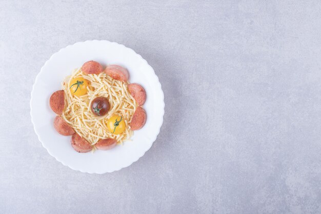 Спагетти с жареными сосисками и помидорами в белой миске.