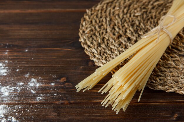 Spaghetti with sprinkled flour on wooden and wicker placemat background, high angle view.