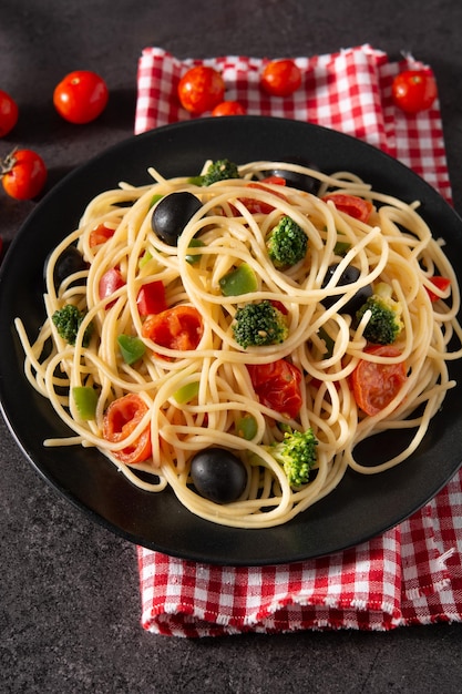 Spaghetti with vegetablesbroccolitomatoespeppers on black slate background