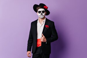 Spanish man with face art on halloween posing in black suit on purple background.