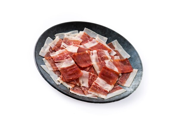 Spanish serrano ham slice on black plate isolated on white background