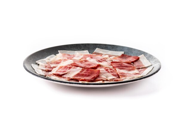 Spanish serrano ham slice on black plate isolated on white background