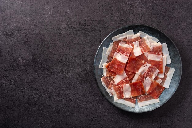 Spanish serrano ham slices on black plate on black slate background