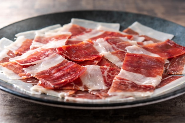 Spanish serrano ham slices on black plate on wooden table