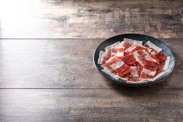 Spanish serrano ham slices on black plate on wooden table