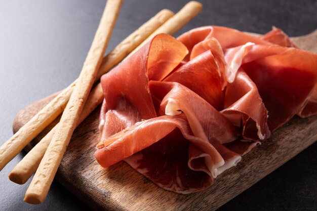 spanish serrano ham with olives and breadstick on black background