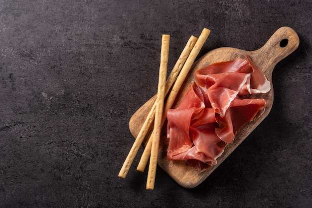 Spanish serrano ham with olives and breadstick on black background