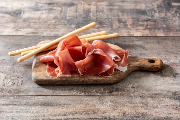 Spanish serrano ham with olives and breadstick on wooden table background