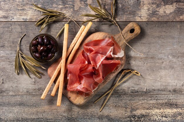 Spanish serrano ham with olives and breadstick on wooden table