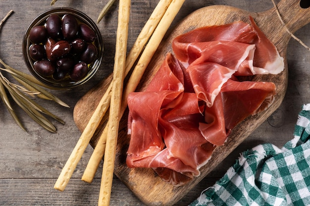 Spanish serrano ham with olives and breadstick on wooden table