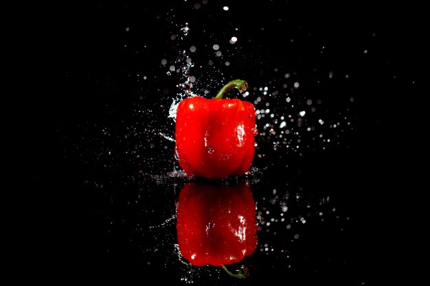 Sparkling water falls on delicious red pepper which stands on black table