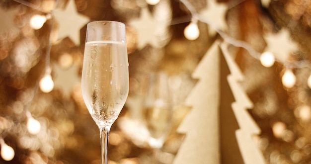 Игристое вино в бокале флейты на фоне стильных рождественских украшений в золотых тонах