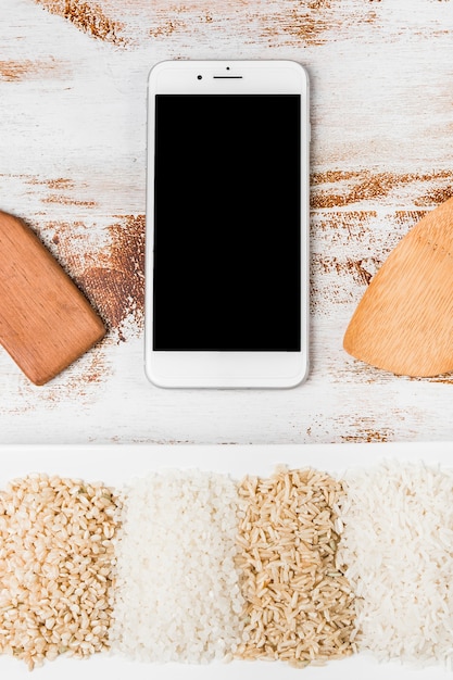 Spatula and mobile phone over the variety of rice on white tray