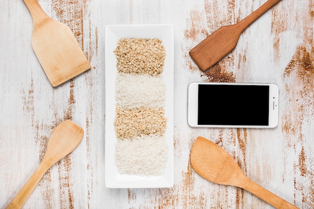 Spatulas; cell phone and tray with variety of rice on grunge background