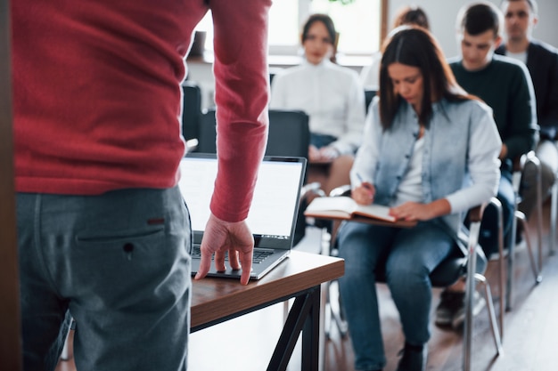 Speaker uses laptop. Group of people at business conference in modern classroom at daytime