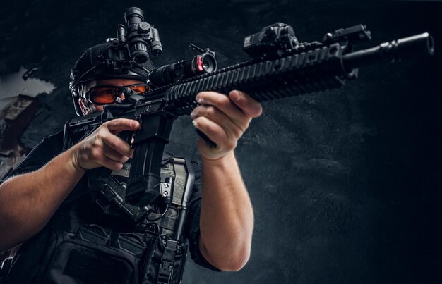 Special forces soldier holding an assault rifle with a laser sight and aims at the target. Studio photo against a dark textured wall