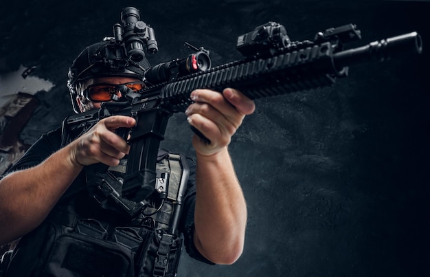 Special forces soldier holding an assault rifle with a laser sight and aims at the target. Studio photo against a dark textured wall
