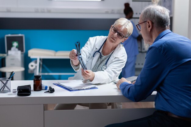 Specialist explaining radiography diagnosis to patient with disease at medical appointment. Healthcare practitioner showing x ray scan results to sick man at annual checkup visit.