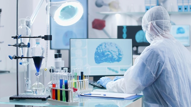 病院​の​実験室​で​の​生化学​実験​で​働く​コンピューター​の​キーボード​を​使用して​医療​の​専門​知識​を​入力する​脳​活動​を​分析する​ppe​機器​を​備えた​専門​の​研究者​。​医学​の​概念