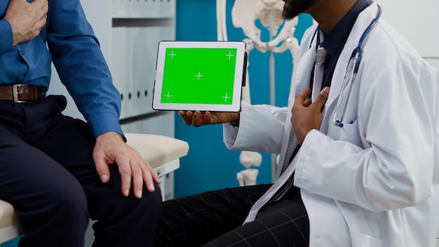 Специалист показывает горизонтальный зеленый экран на планшете пожилому пациенту, глядя на дисплей с цветным ключом. Пожилой человек и врач используют пустой шаблон макета с копирайтом. Закрыть.