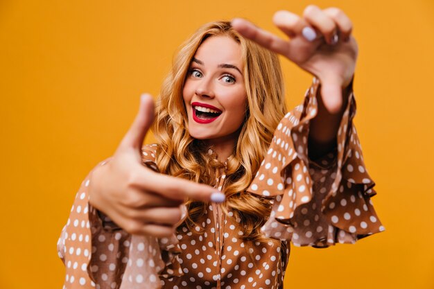 Spectacular blue-eyed woman posing on yellow wall. Indoor shot of debonair girl fooling around during photoshoot.