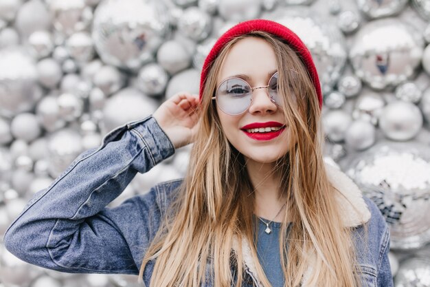 Spectacular girl in denim jacket  through blue glasses. Photo of joyful lady with straight hairstyle smiling on sparkle wall.