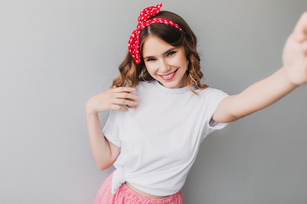 Spettacolare ragazza in nastro rosso in posa giocosamente. adorabile signora con un sorriso sincero che fa selfie.