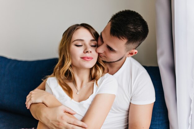 Spectacular girl in white t-shirt spending weekend with boyfriend. Joyful man kissing wife in morning.