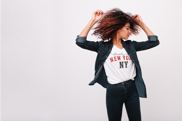 Spectacular lady in black pants funny dancing with hands up and calm face expression. Indoor portrait of active slim girl with brown curly hair enjoying music