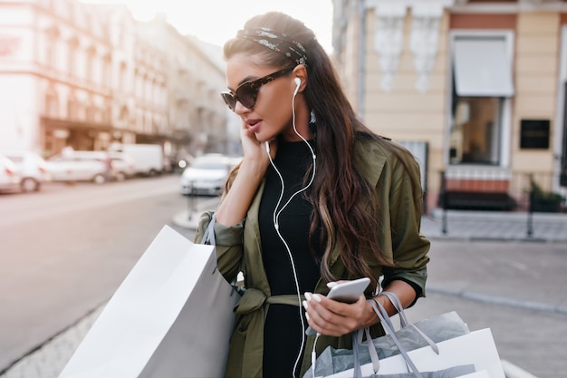 Free photo spectacular latin woman in stylish sunglasses chilling in city and listening music in earphones