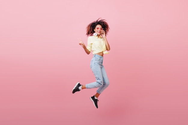 Free photo spectacular sporty woman with brown skin dancing with happy face. adorable mulatto girl in black sneakers expressing positive emotions.