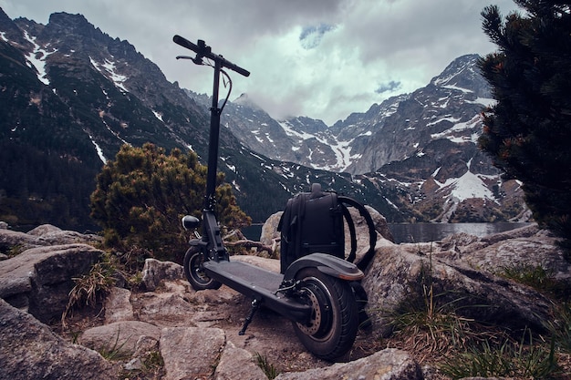 Foto gratuita spettacolare vista su montagne, pini e nuvole basse e cupe con zaino e scooter nella parte anteriore.