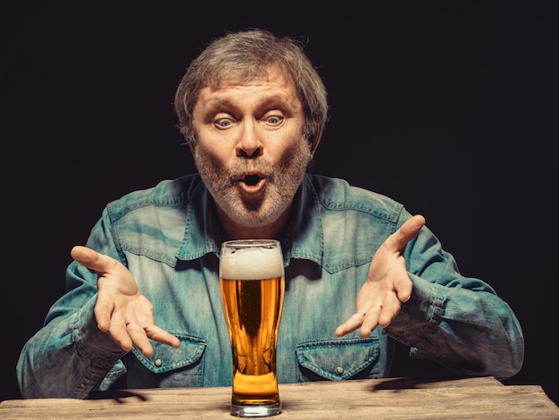 The spellbound man in denim shirt with glass of beer