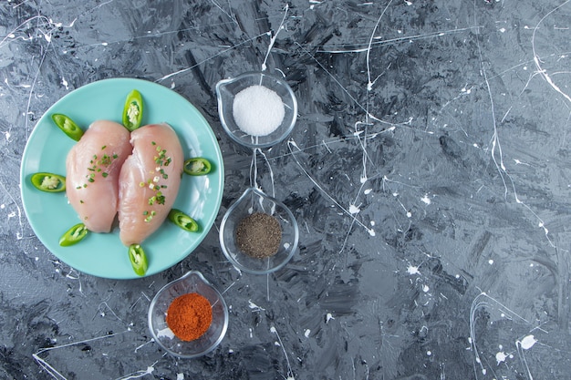 Чаши для специй и куриная грудка на тарелке, на мраморном фоне.
