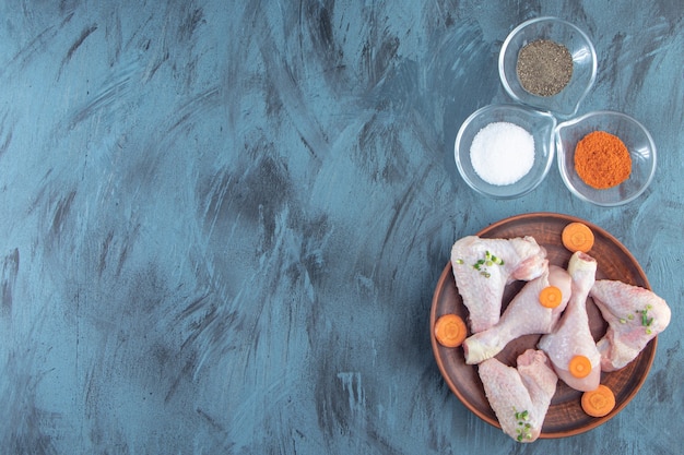 Foto gratuita ciotole di spezie e carne di pollo su un piatto di legno, sullo sfondo blu.