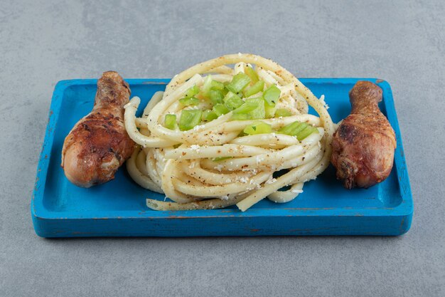 Spiced spaghetti and chicken chicken legs on blue plate.