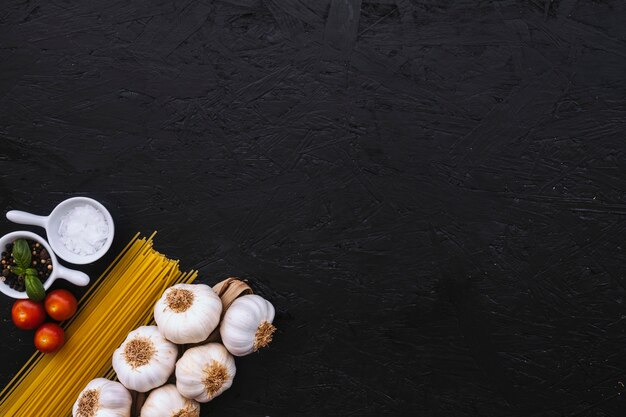 Spices and tomatoes near spaghetti and garlic