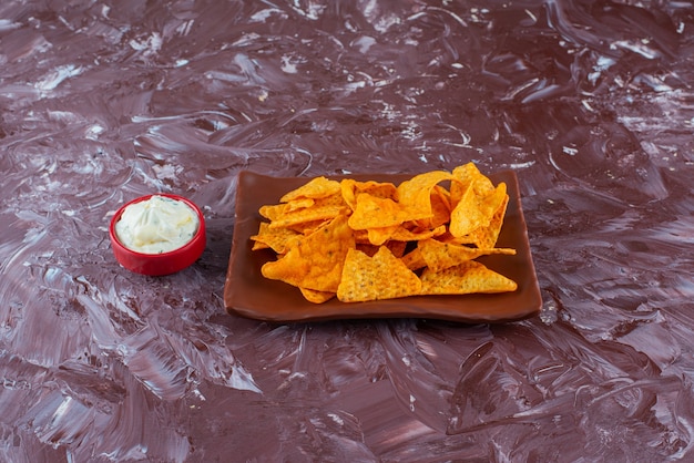 Spicy chips on a plate next to a bowl of mayonnaise , on the marble table. 