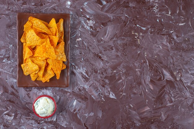 Spicy chips on a plate next to a bowl of mayonnaise , on the marble table. 