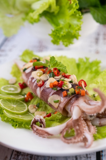 Spicy lemon squid with galangal, chilies, carrots, peppermint, spring onions and garlic on a plate on a white wooden floor.