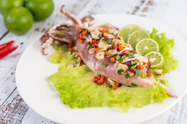 Spicy lemon squid with galangal, chilies, carrots, peppermint, spring onions and garlic on a plate on a white wooden floor.