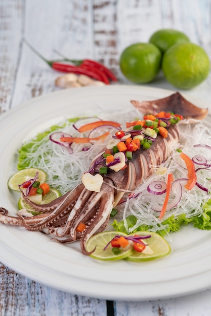 Spicy lemon squid with galangal, chilies, carrots, peppermint, spring onions and garlic on a plate on a white wooden floor.