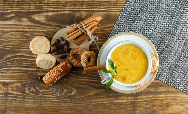 Spicy milk in a cup with mint, biscuits, cloves, cinnamon sticks top view on wooden table