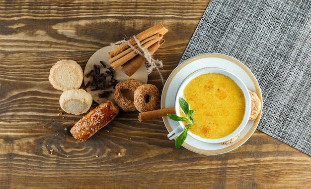 Spicy milk in a cup with mint, biscuits, cloves, cinnamon sticks top view on wooden table