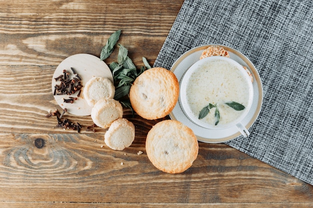 Spicy milk in a cup with mint, cookies, cloves top view on wooden table