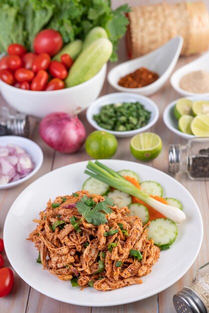 Spicy minced chicken on a white plate complete with cucumber, lettuce and side dishes.