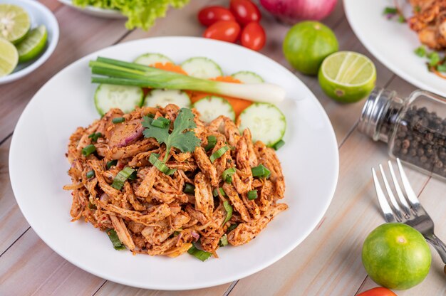 Spicy minced chicken on a white plate complete with cucumber, lettuce and side dishes.