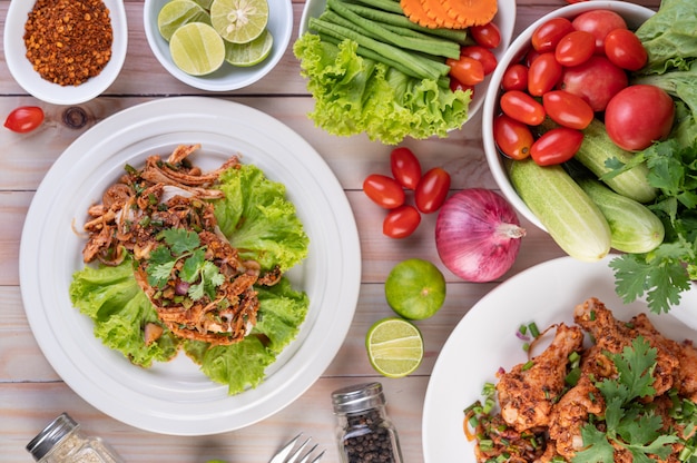 Spicy minced chicken on a white plate complete with cucumber, lettuce and side dishes.