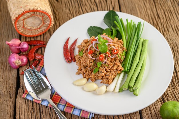 Spicy Minced Pork Salad on a white plate with lentils, kaffir lime leaves and spring onions.