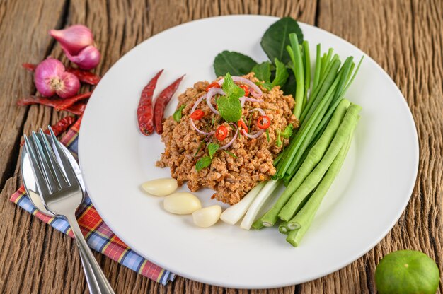 Spicy Minced Pork Salad on a white plate with lentils, kaffir lime leaves and spring onions.